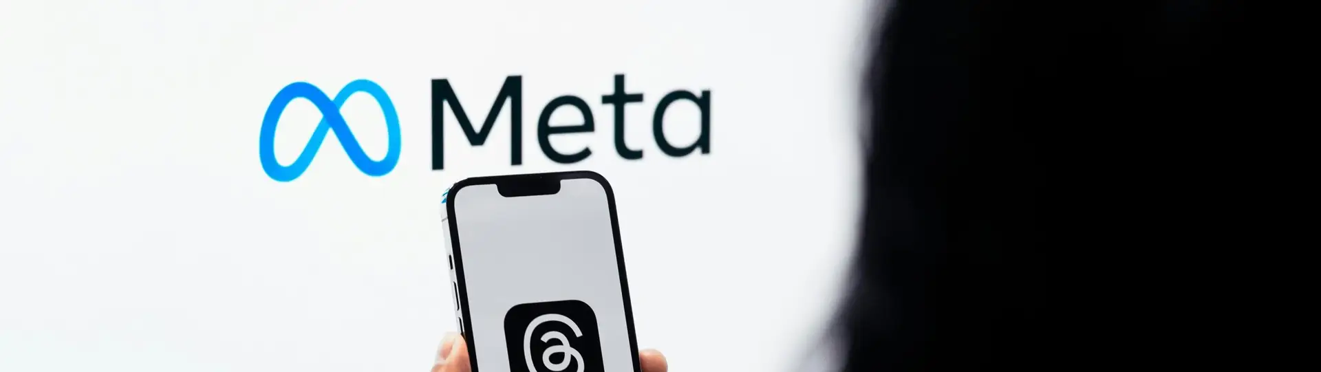 Hands holding smartphone with Meta Threads logo on screen, Meta branding in background.